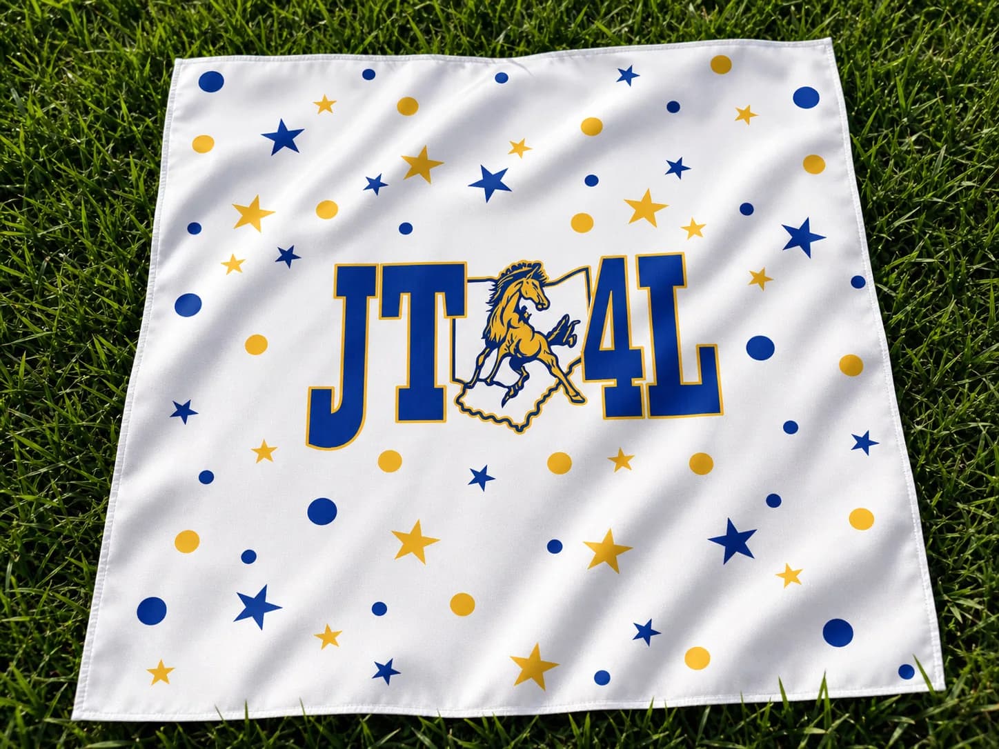 White alma mater bandana with blue and gold stars displayed on grass